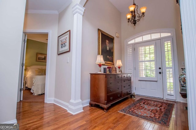 entryway featuring crown molding, hardwood / wood-style flooring, baseboards, a chandelier, and ornate columns