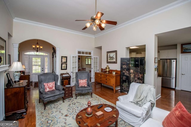 living area with crown molding, wood finished floors, ornate columns, arched walkways, and ceiling fan with notable chandelier