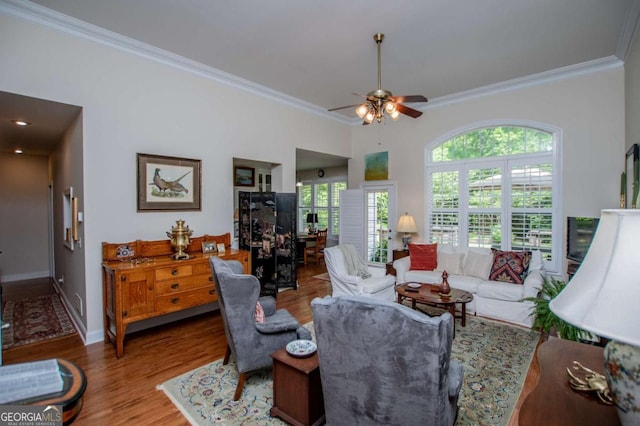 living area featuring baseboards, ornamental molding, a ceiling fan, and wood finished floors