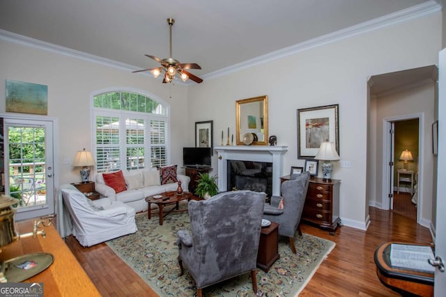 living area with crown molding, wood finished floors, a fireplace, baseboards, and ceiling fan