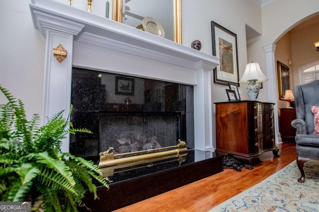 living area featuring crown molding, arched walkways, wood finished floors, and a fireplace
