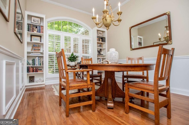 dining room featuring wood-type flooring, ornamental molding, built in features, baseboards, and a notable chandelier