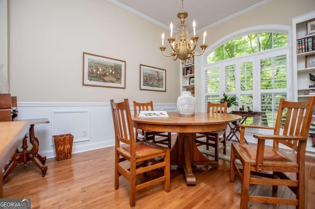 dining area featuring crown molding, wainscoting, light wood-type flooring, and a chandelier