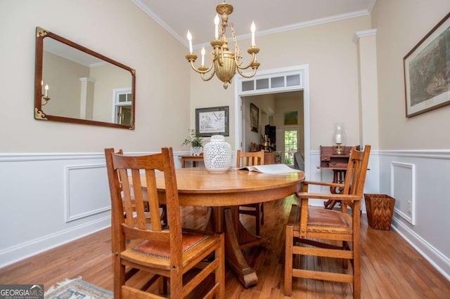 dining space featuring an inviting chandelier, wainscoting, crown molding, and wood finished floors