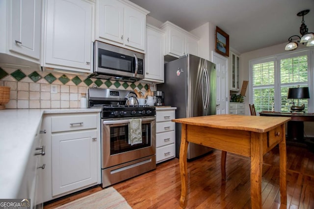 kitchen with white cabinets, appliances with stainless steel finishes, light wood finished floors, light countertops, and tasteful backsplash