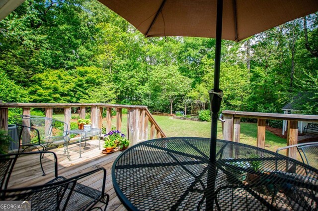 wooden deck featuring outdoor dining area, a lawn, central AC, and a forest view