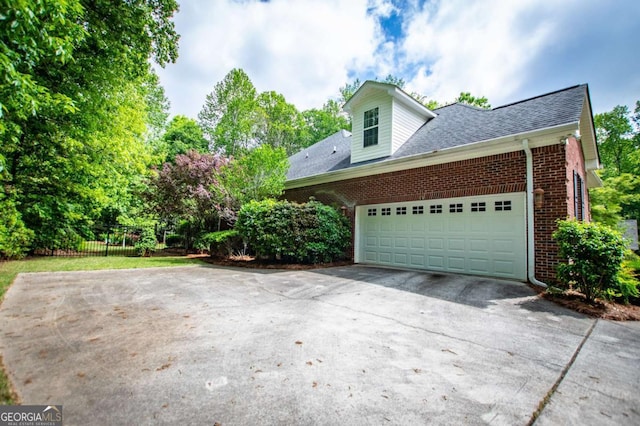 view of home's exterior with fence, roof with shingles, an attached garage, brick siding, and driveway