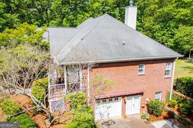 view of side of property featuring a chimney, brick siding, concrete driveway, an attached garage, and a shingled roof