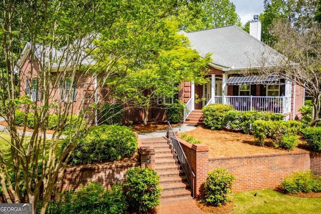 view of front of home with covered porch, brick siding, stairway, and a chimney