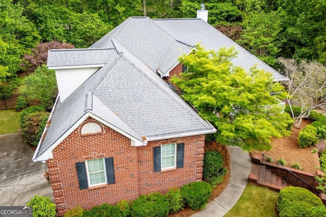 view of side of property with brick siding, roof with shingles, fence, and a chimney