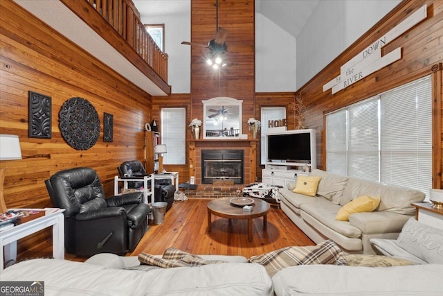 living area featuring a brick fireplace, high vaulted ceiling, a ceiling fan, wood walls, and hardwood / wood-style flooring