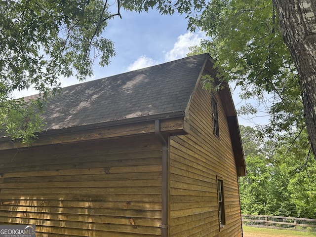 exterior space featuring a downspout, gutters, a shingled roof, and fence