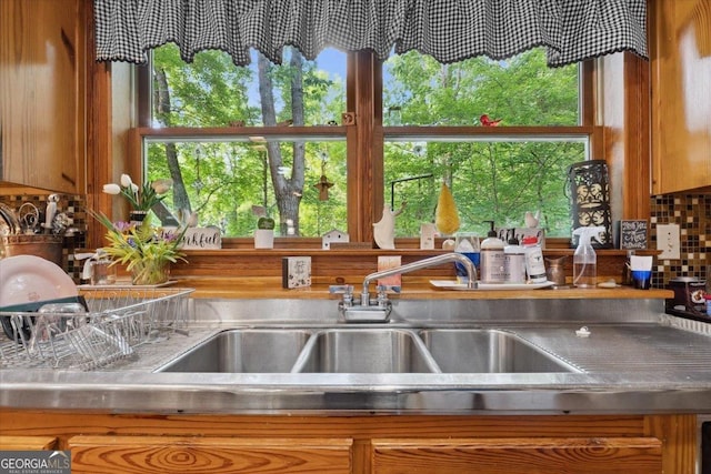 kitchen featuring tasteful backsplash, a sink, stainless steel countertops, and brown cabinets