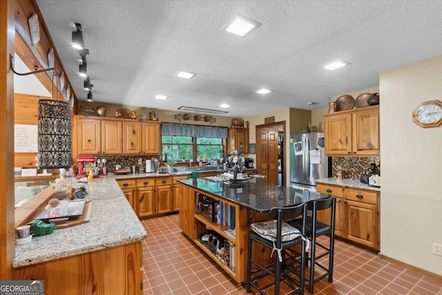 kitchen featuring freestanding refrigerator, backsplash, a kitchen bar, a center island, and a textured ceiling