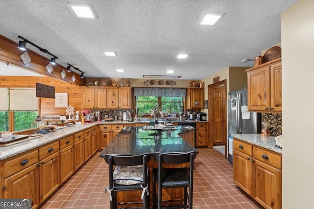 kitchen with a breakfast bar, a textured ceiling, freestanding refrigerator, and a kitchen island