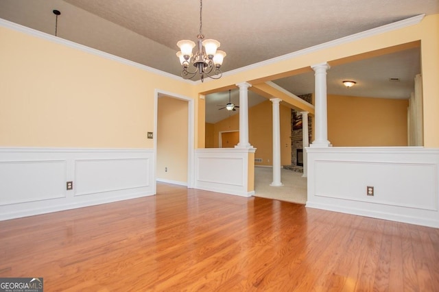 unfurnished dining area with wood finished floors, decorative columns, ornamental molding, ceiling fan with notable chandelier, and a wainscoted wall