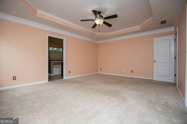 empty room with visible vents, a tray ceiling, carpet floors, ornamental molding, and a ceiling fan