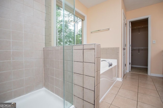 full bath with tiled shower, tile patterned floors, a walk in closet, baseboards, and a garden tub
