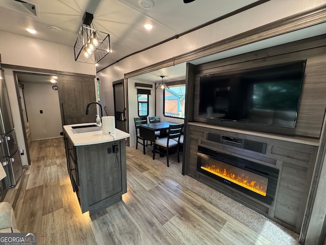 kitchen with a center island with sink, a sink, light countertops, light wood finished floors, and a glass covered fireplace