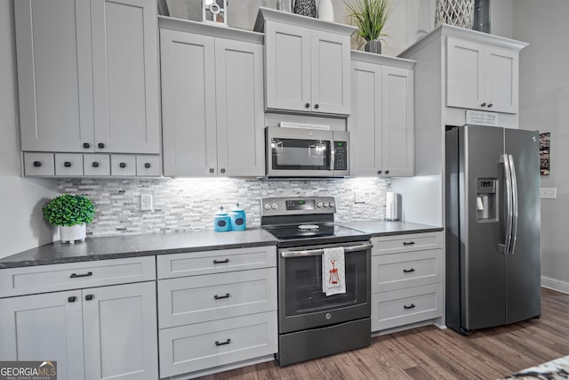 kitchen with dark wood-style floors, dark countertops, appliances with stainless steel finishes, and tasteful backsplash