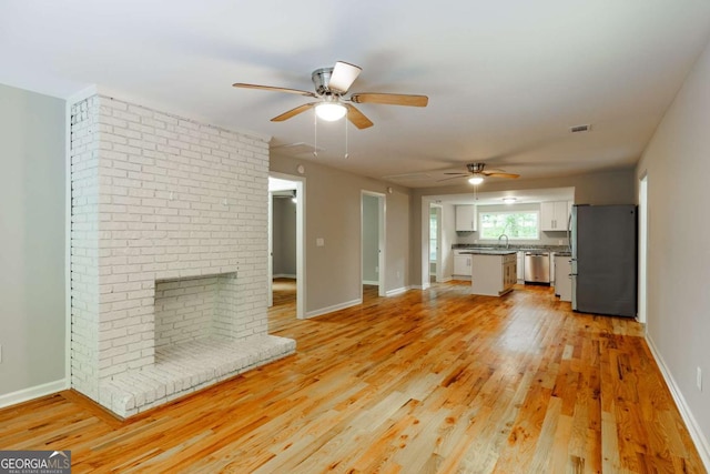 unfurnished living room with visible vents, ceiling fan, light wood-style flooring, and a sink
