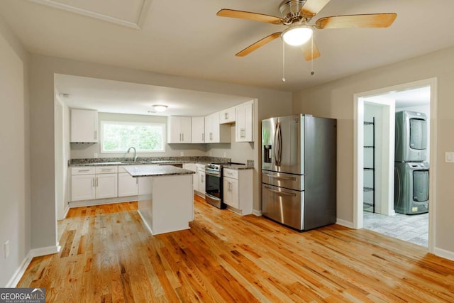 kitchen with light wood-style flooring, stacked washing maching and dryer, stainless steel appliances, and white cabinetry