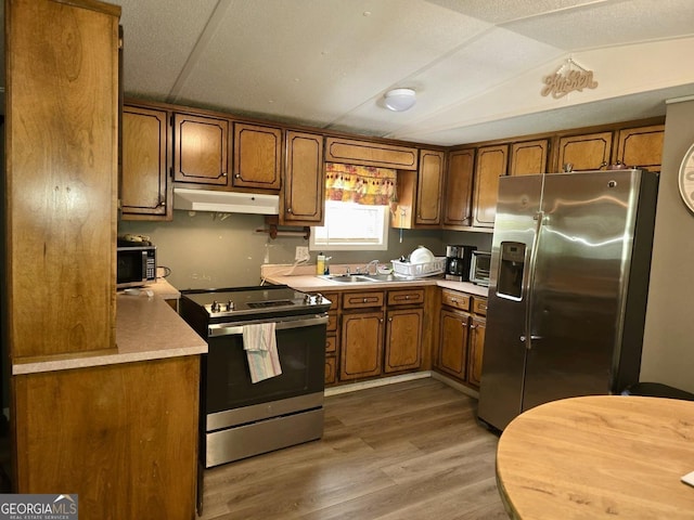 kitchen with brown cabinets, light countertops, stainless steel appliances, light wood-type flooring, and under cabinet range hood