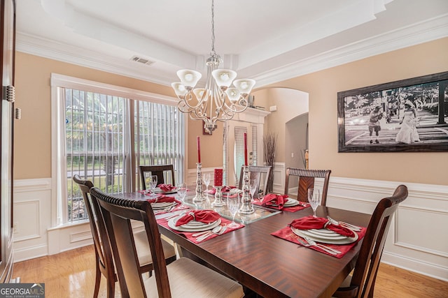 dining room with visible vents, a chandelier, a tray ceiling, arched walkways, and light wood finished floors