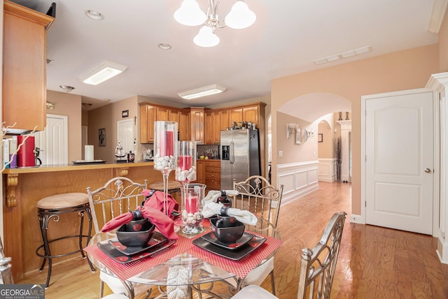 dining space with visible vents, arched walkways, light wood-type flooring, a notable chandelier, and wainscoting