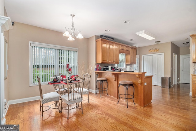 kitchen with a chandelier, light wood-style floors, a kitchen breakfast bar, a peninsula, and baseboards