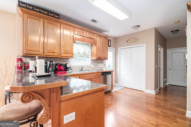 kitchen featuring light wood finished floors, a sink, decorative backsplash, visible vents, and stainless steel dishwasher