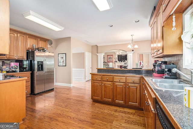 kitchen with a sink, stainless steel refrigerator with ice dispenser, backsplash, ornate columns, and arched walkways