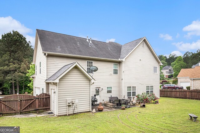rear view of property with fence, a gate, a patio area, an attached garage, and a lawn