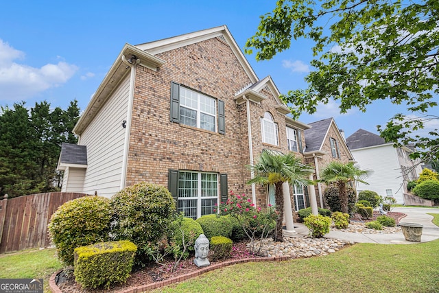 view of front of house with brick siding, fence, and a front lawn