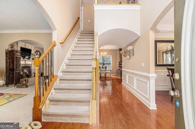 foyer entrance featuring crown molding, a warm lit fireplace, arched walkways, wood finished floors, and stairs