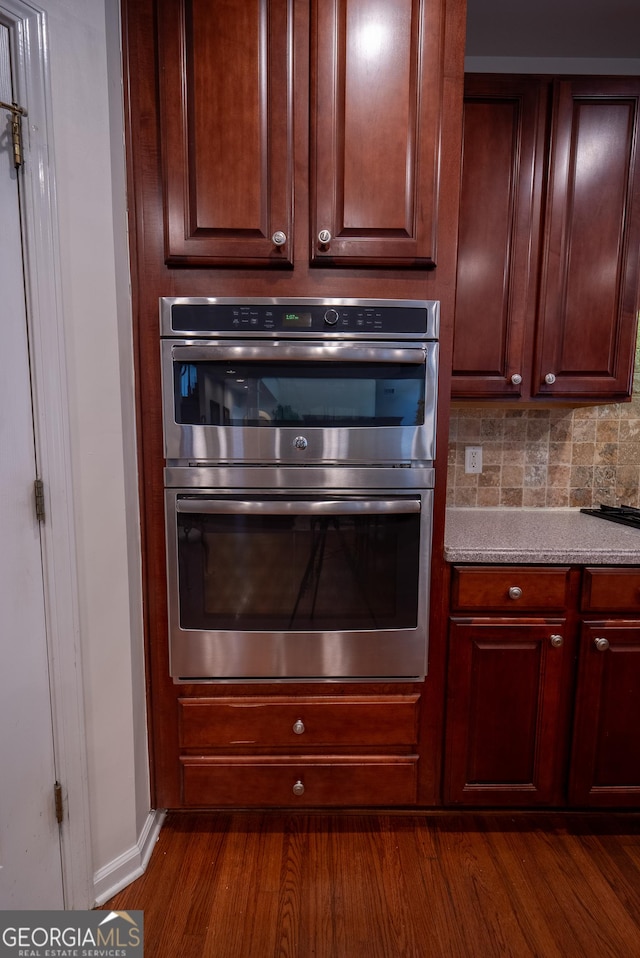 kitchen with baseboards, dark wood-style floors, stainless steel double oven, light countertops, and tasteful backsplash