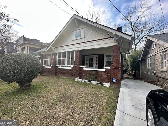 view of front of house with brick siding, a front yard, covered porch, and a chimney