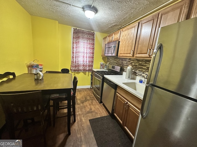 kitchen featuring dark wood-style flooring, stainless steel appliances, backsplash, light countertops, and a textured ceiling