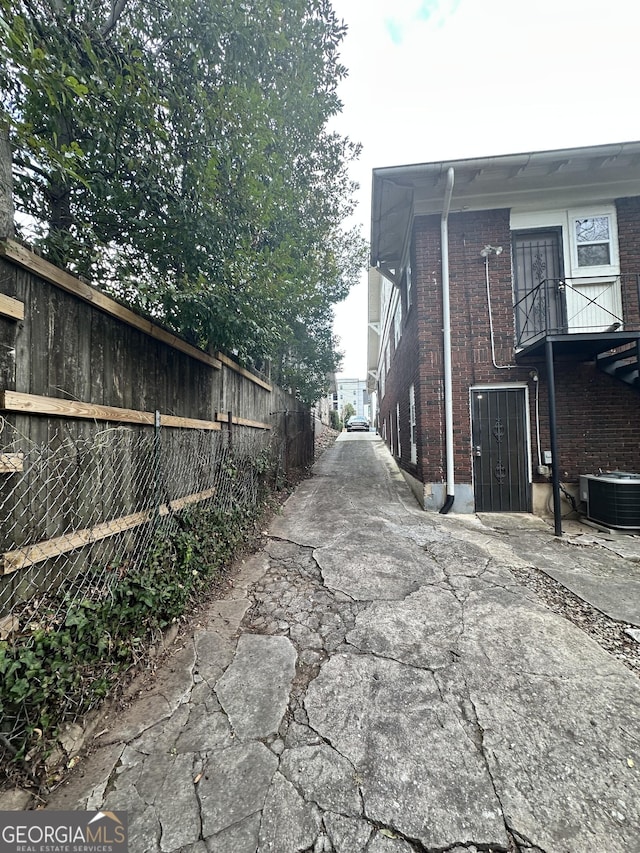 view of side of property featuring brick siding, central AC, a balcony, and fence