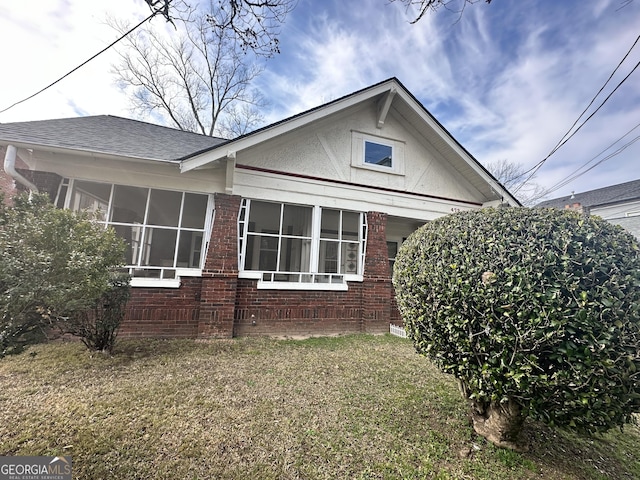 view of property exterior with brick siding, a shingled roof, a sunroom, and a lawn