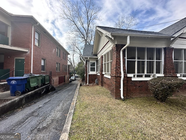 view of home's exterior with a yard, a shingled roof, and brick siding