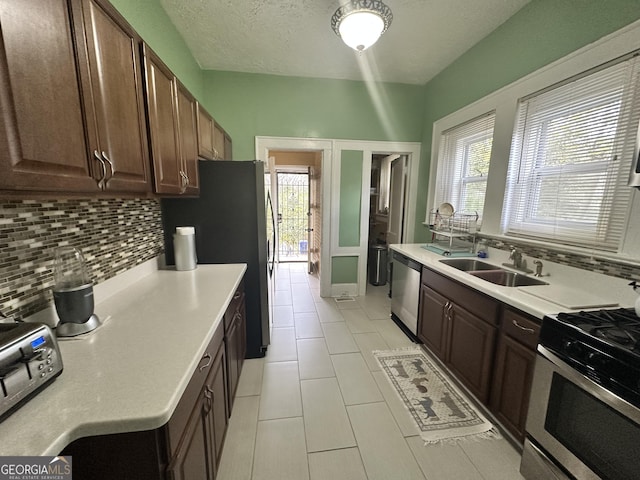 kitchen with a sink, appliances with stainless steel finishes, light countertops, dark brown cabinetry, and backsplash