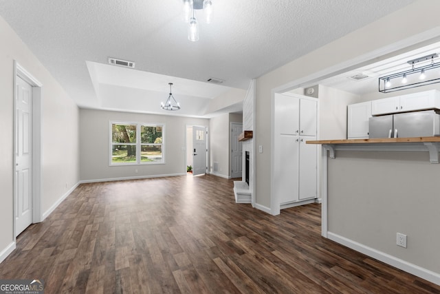 unfurnished living room with dark wood-type flooring, visible vents, a notable chandelier, and baseboards