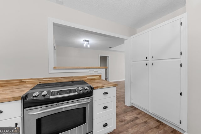 kitchen featuring wood finished floors, wooden counters, stainless steel range with electric cooktop, and white cabinets