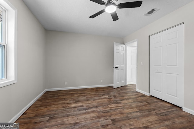 unfurnished bedroom with dark wood finished floors, a closet, ceiling fan, baseboards, and visible vents