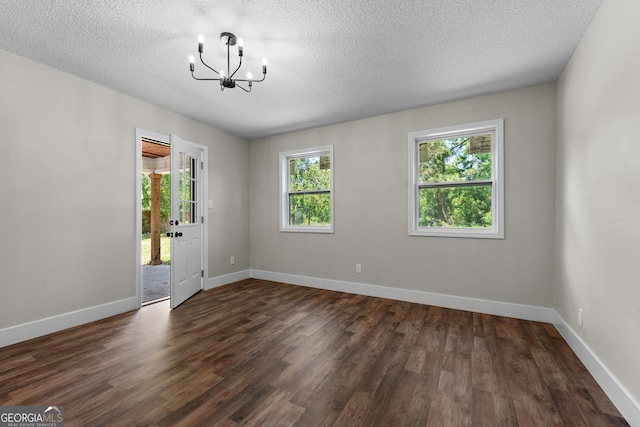 empty room with a textured ceiling, a notable chandelier, baseboards, and dark wood-type flooring