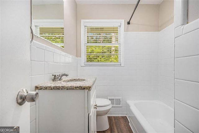 bathroom with tile walls, washtub / shower combination, vanity, toilet, and visible vents
