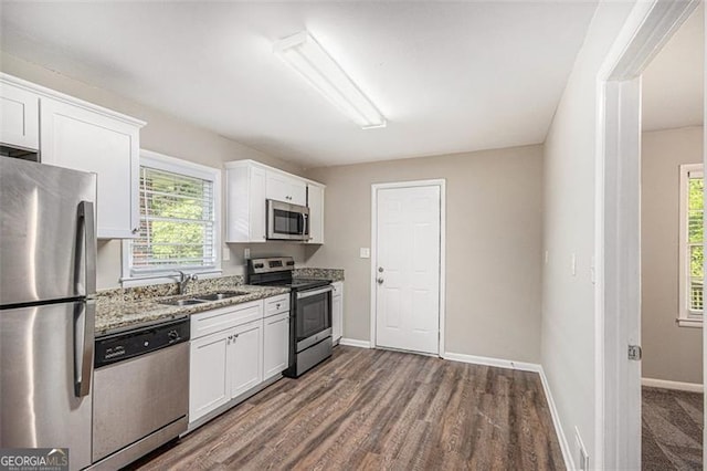 kitchen with baseboards, light stone countertops, appliances with stainless steel finishes, a sink, and white cabinetry
