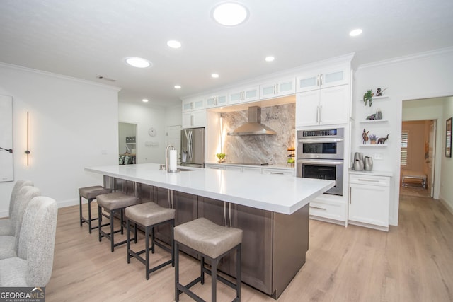 kitchen with a large island, crown molding, white cabinetry, wall chimney range hood, and appliances with stainless steel finishes