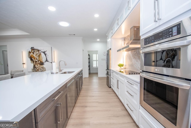 kitchen with appliances with stainless steel finishes, wall chimney range hood, light countertops, and a sink